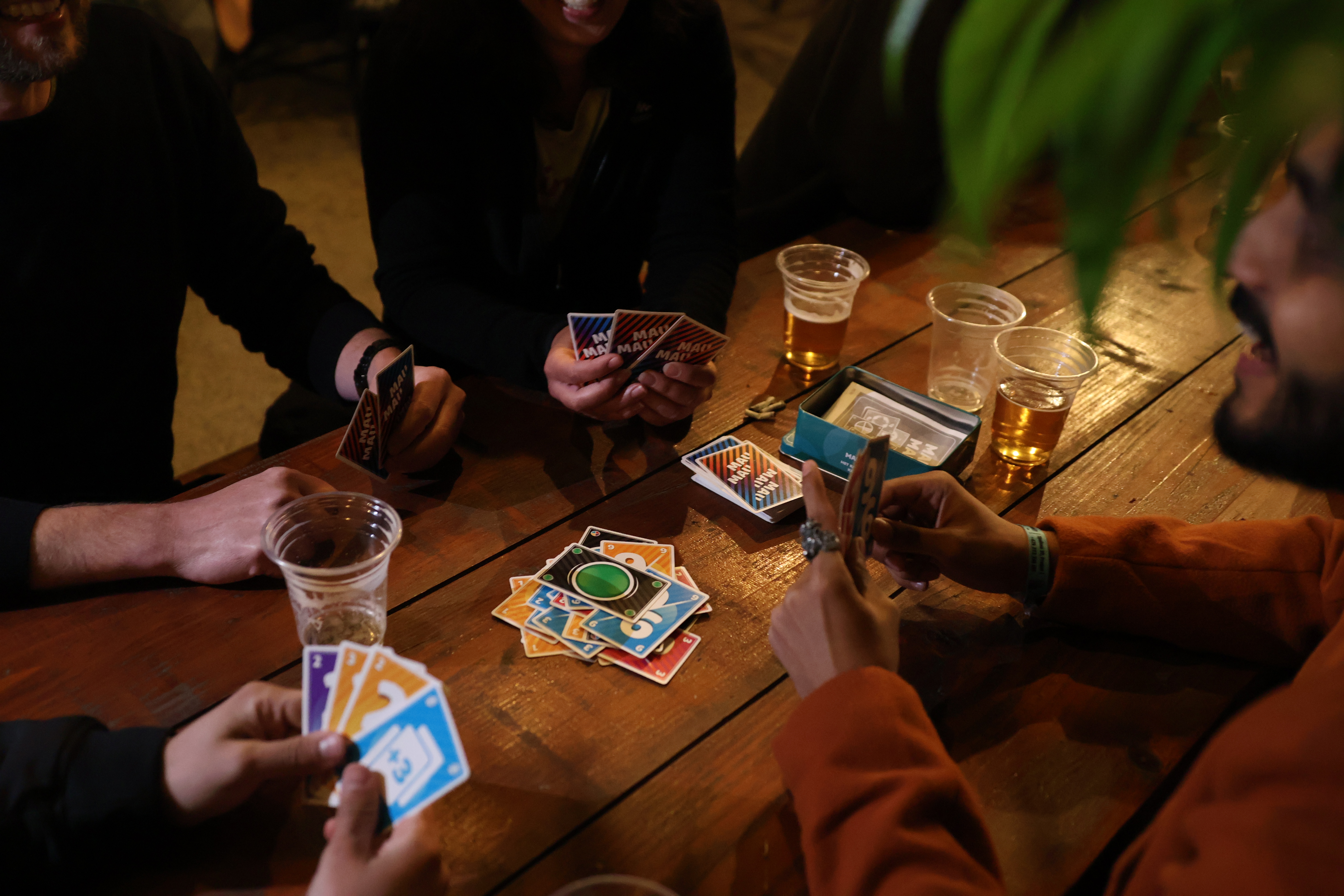 A group of people playing a card game around a wooden table.