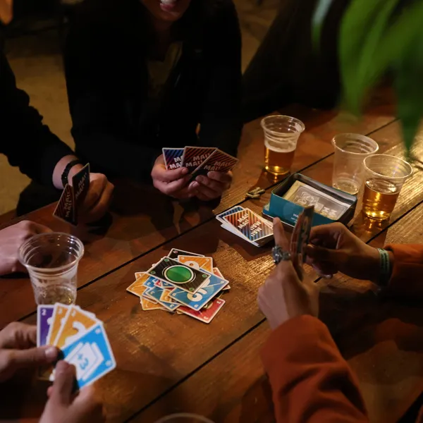 A group of people playing a card game around a wooden table.