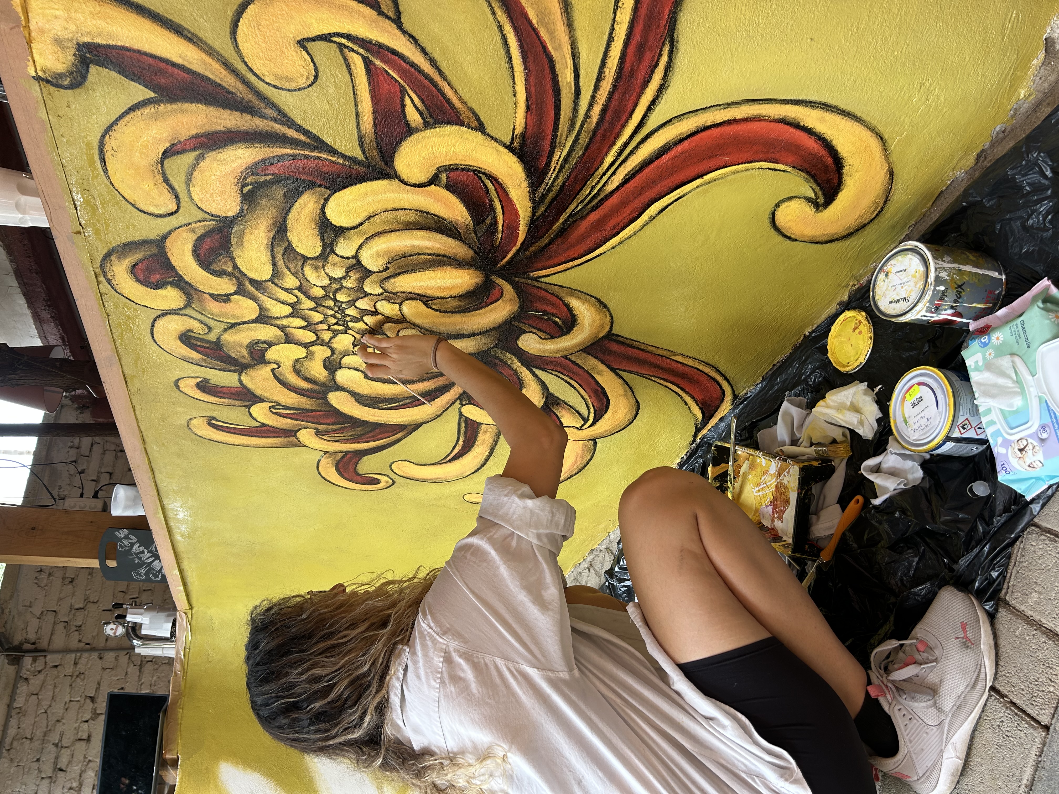 A person painting a large yellow flower mural on a wall.