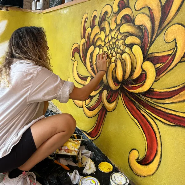 A person painting a large yellow flower mural on a wall.