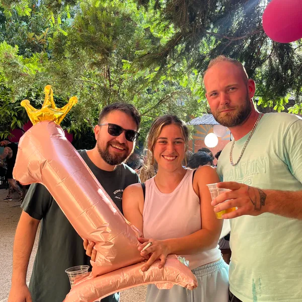 Three friends posing outdoors with a pink number one balloon.